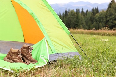 Photo of Trekking shoes and camping tent on green grass outdoors, space for text