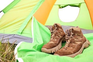 Photo of Trekking shoes and camping tent on green grass outdoors