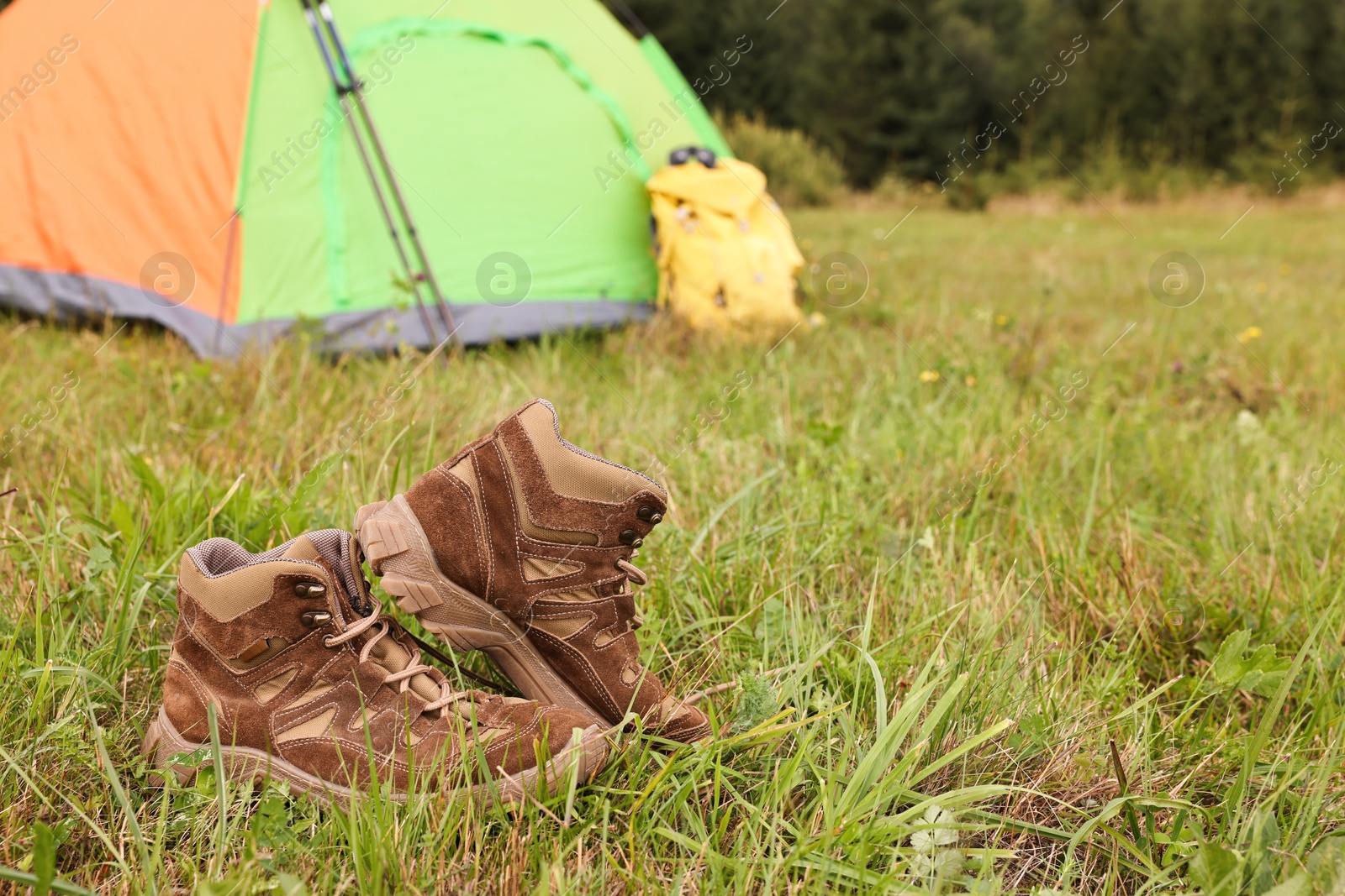 Photo of Trekking shoes and camping tent on green grass outdoors, space for text