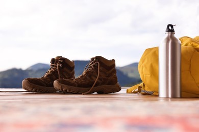 Trekking shoes, backpack and thermos on wooden table