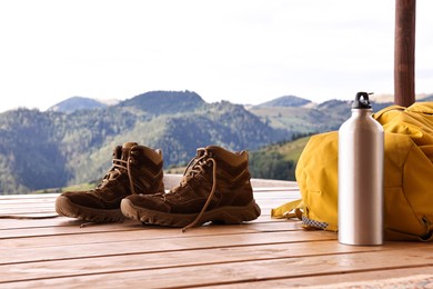 Trekking shoes, backpack and thermos on wooden table