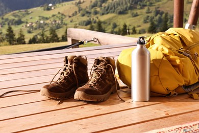 Photo of Trekking shoes, backpack and thermos on wooden table