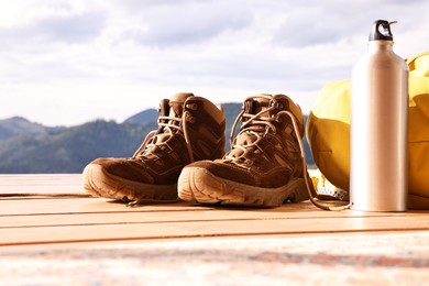 Trekking shoes, backpack and thermos on wooden table