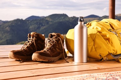 Trekking shoes, backpack and thermos on wooden table