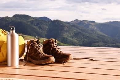 Trekking shoes, backpack and thermos on wooden table, space for text