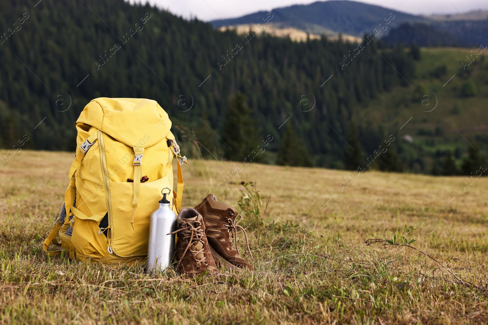 Photo of Backpack, thermos and trekking shoes on grass outdoors, space for text