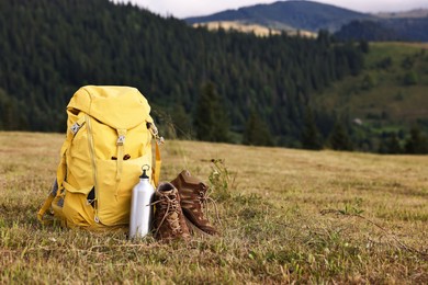 Backpack, thermos and trekking shoes on grass outdoors, space for text