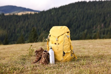 Backpack, thermos and trekking shoes on grass outdoors