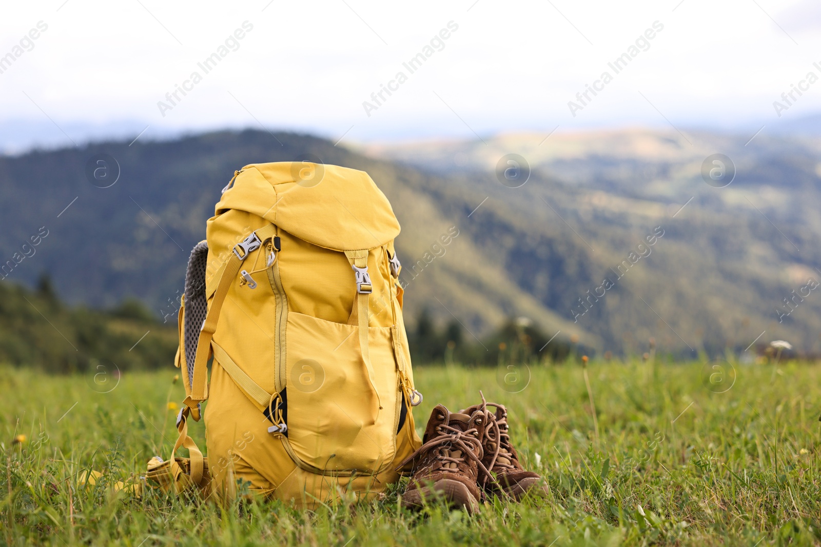 Photo of Backpack and trekking shoes on green grass outdoors, space for text