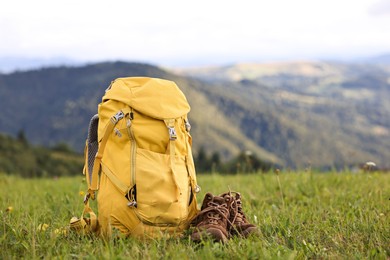 Photo of Backpack and trekking shoes on green grass outdoors, space for text