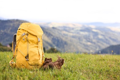 Photo of Backpack and trekking shoes on green grass outdoors, space for text