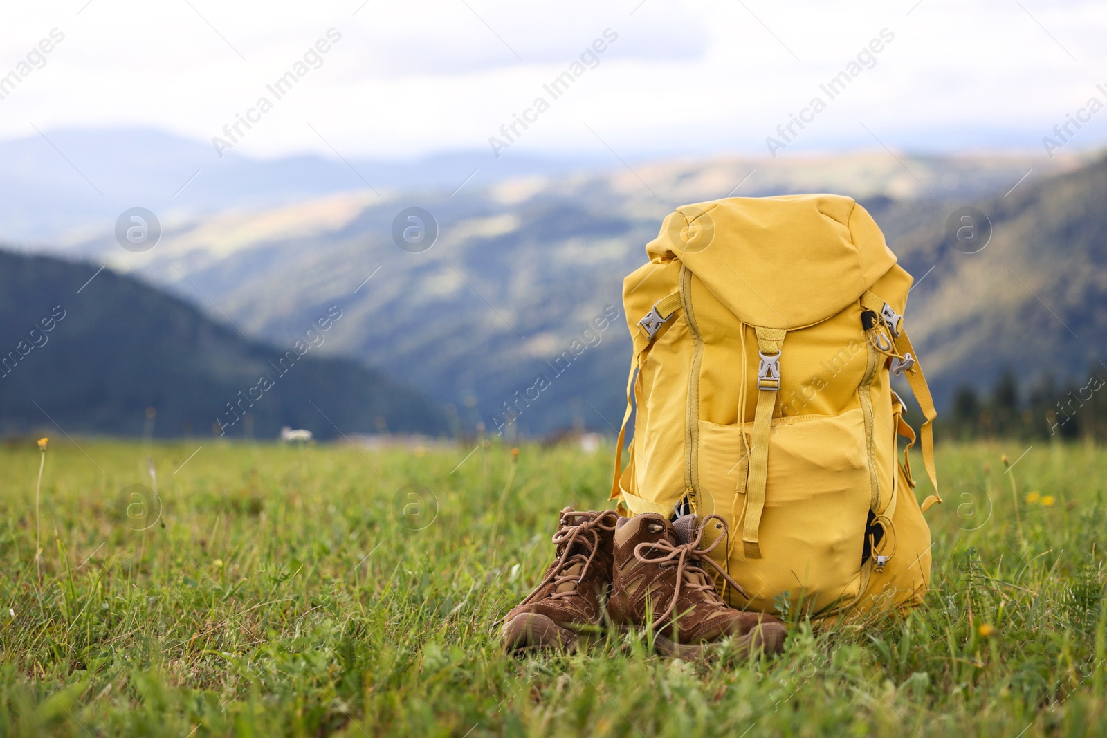 Photo of Backpack and trekking shoes on green grass outdoors, space for text