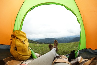 Woman wearing trekking shoes and lying in tent outdoors, closeup. Fisheye lens effect