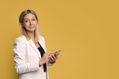 Photo of Beautiful smiling woman using smartphone on yellow background, space for text