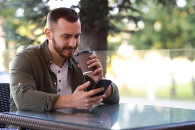 Handsome man using smartphone and drinking coffee at outdoor cafe