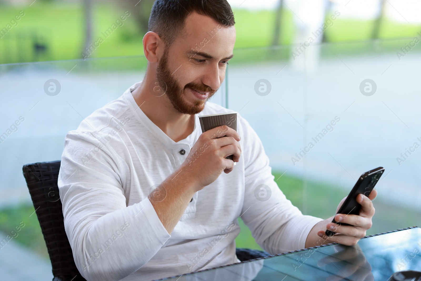 Photo of Handsome man using smartphone and drinking coffee at outdoor cafe