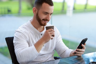 Handsome man using smartphone and drinking coffee at outdoor cafe