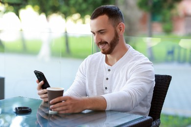 Photo of Happy man using smartphone and drinking coffee at outdoor cafe