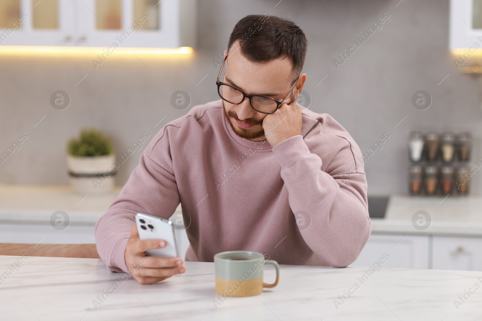 Photo of Handsome man using smartphone at white table in kitchen