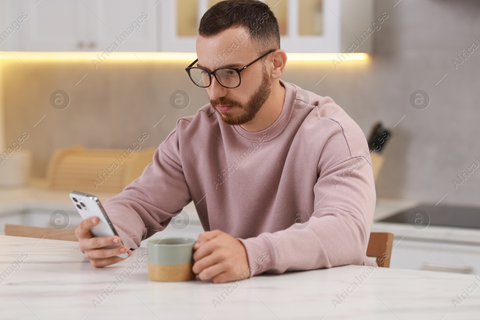 Photo of Handsome man using smartphone at white table in kitchen