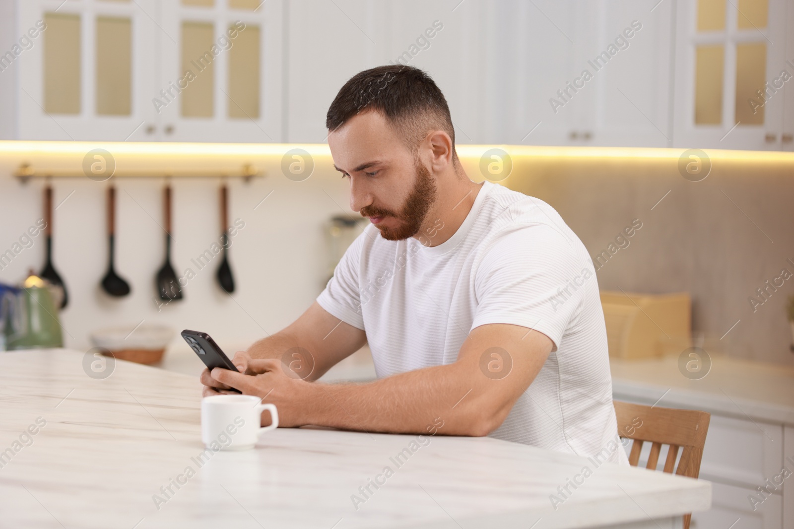 Photo of Handsome man using smartphone at white table in kitchen