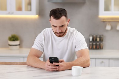 Photo of Handsome man using smartphone at white table in kitchen