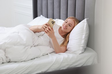 Photo of Smiling woman looking at smartphone in bed