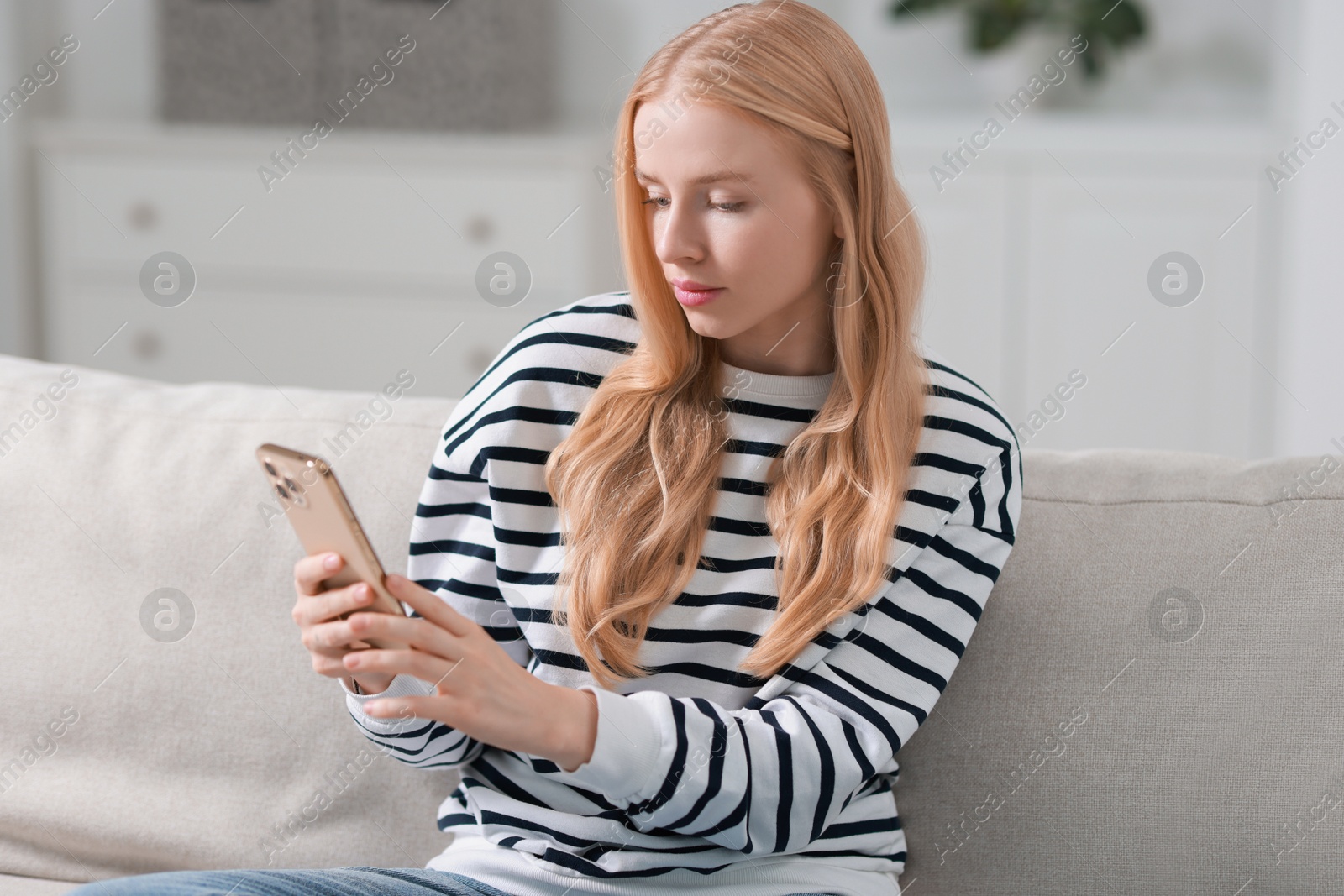 Photo of Beautiful woman using smartphone on sofa indoors