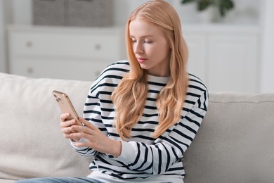 Beautiful woman using smartphone on sofa indoors