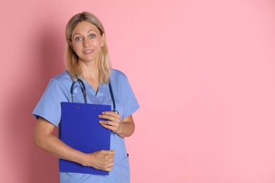 Portrait of doctor in medical uniform with stethoscope and clipboard on pink background, space for text