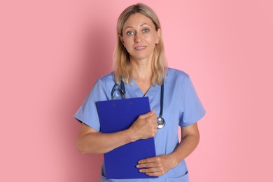 Portrait of doctor in medical uniform with stethoscope and clipboard on pink background