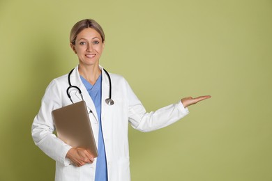 Doctor in medical uniform with stethoscope and laptop on light green background