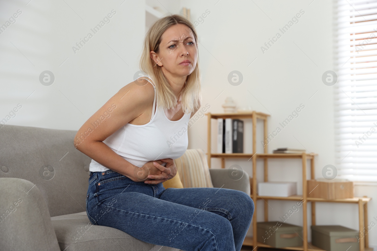 Photo of Menopause. Woman suffering from abdominal pain on sofa at home