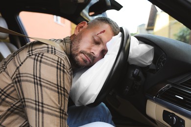 Photo of Unconscious man with head injury on airbag in automobile after car accident