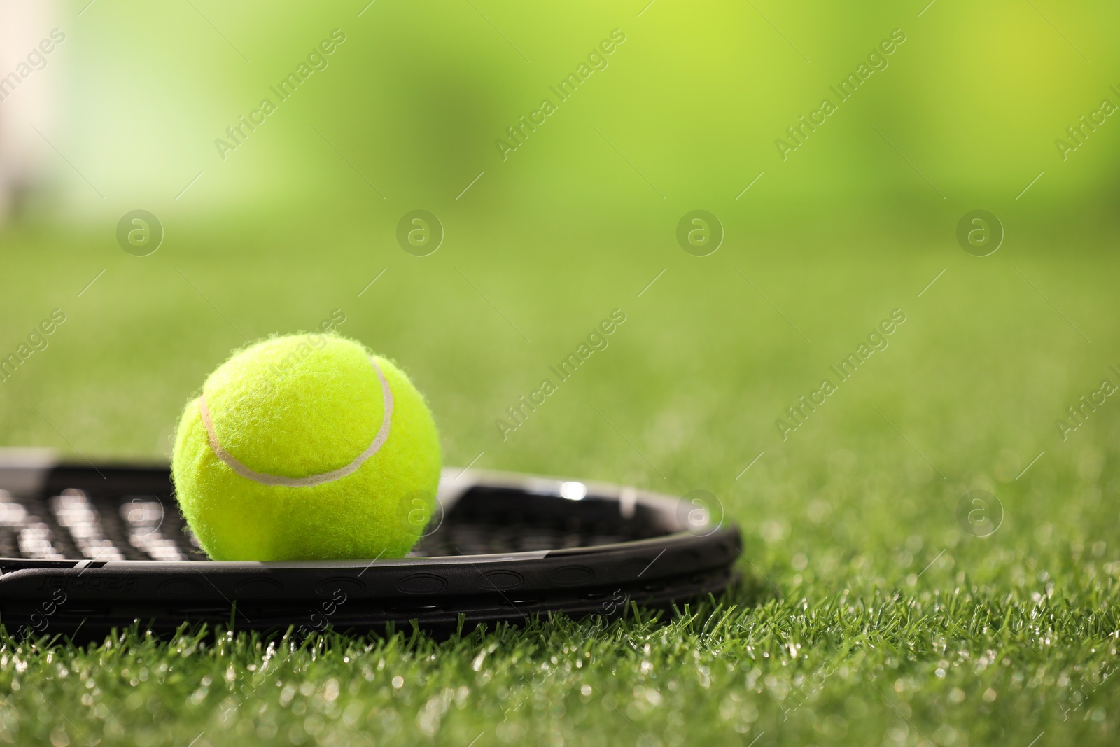 Photo of Tennis racket and ball on green artificial grass, closeup. Space for text