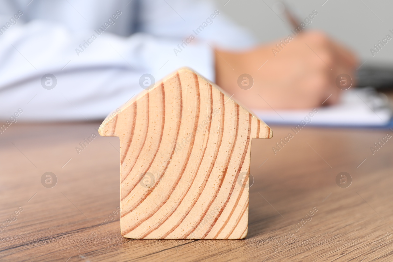 Photo of Real estate insurance. Man writing something at table, focus on wooden house figure