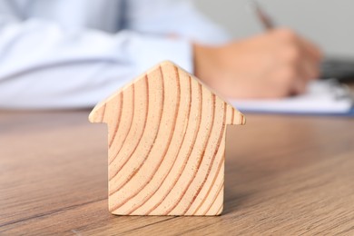 Photo of Real estate insurance. Man writing something at table, focus on wooden house figure