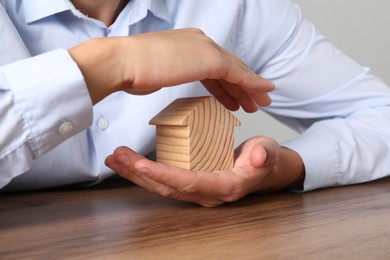 Photo of Real estate insurance. Man with wooden house figure at table, closeup