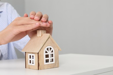 Photo of Real estate insurance. Man with wooden house figure at light table, closeup. Space for text