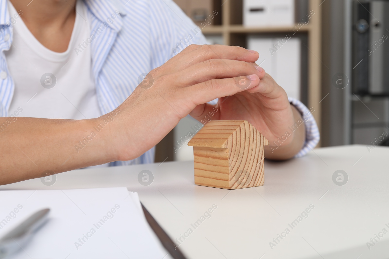 Photo of Real estate insurance. Man with wooden house figure at light table, closeup