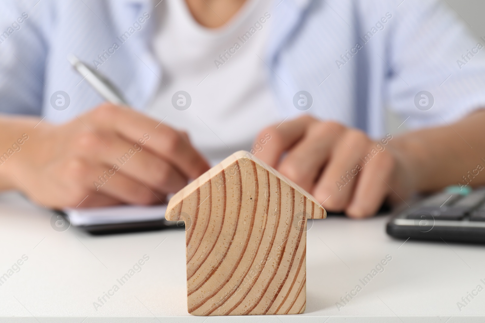 Photo of Real estate insurance. Man writing something at light table, focus on wooden house figure