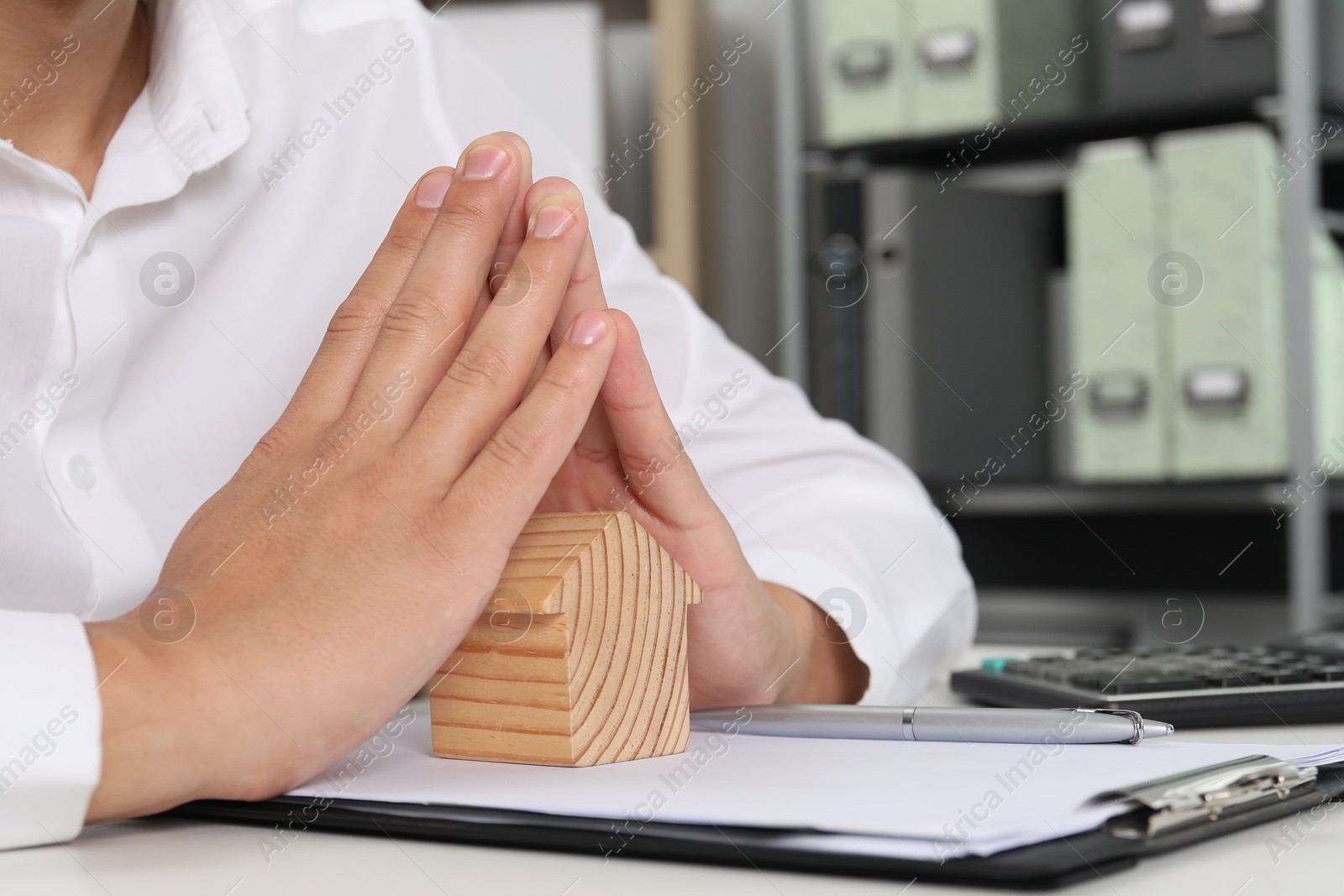 Photo of Real estate insurance. Man with wooden house figure at light table, closeup