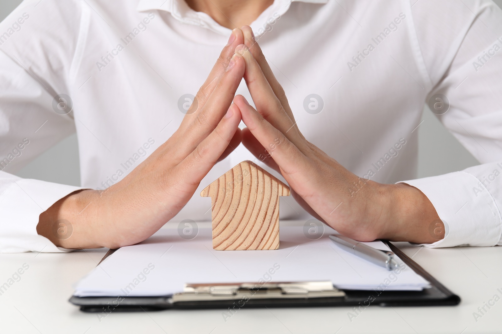 Photo of Real estate insurance. Man with wooden house figure at light table, closeup