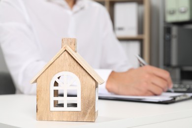 Photo of Real estate insurance. Man writing something at light table, focus on wooden house figure