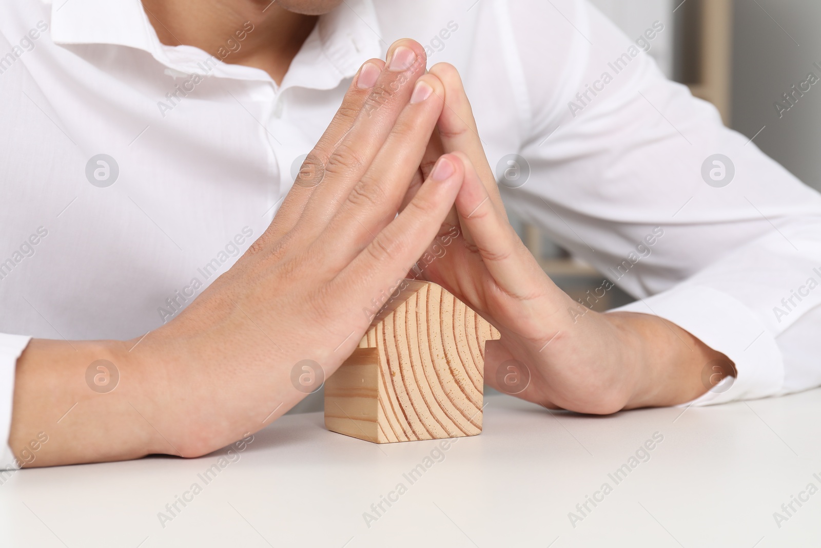 Photo of Real estate insurance. Man with wooden house figure at light table, closeup