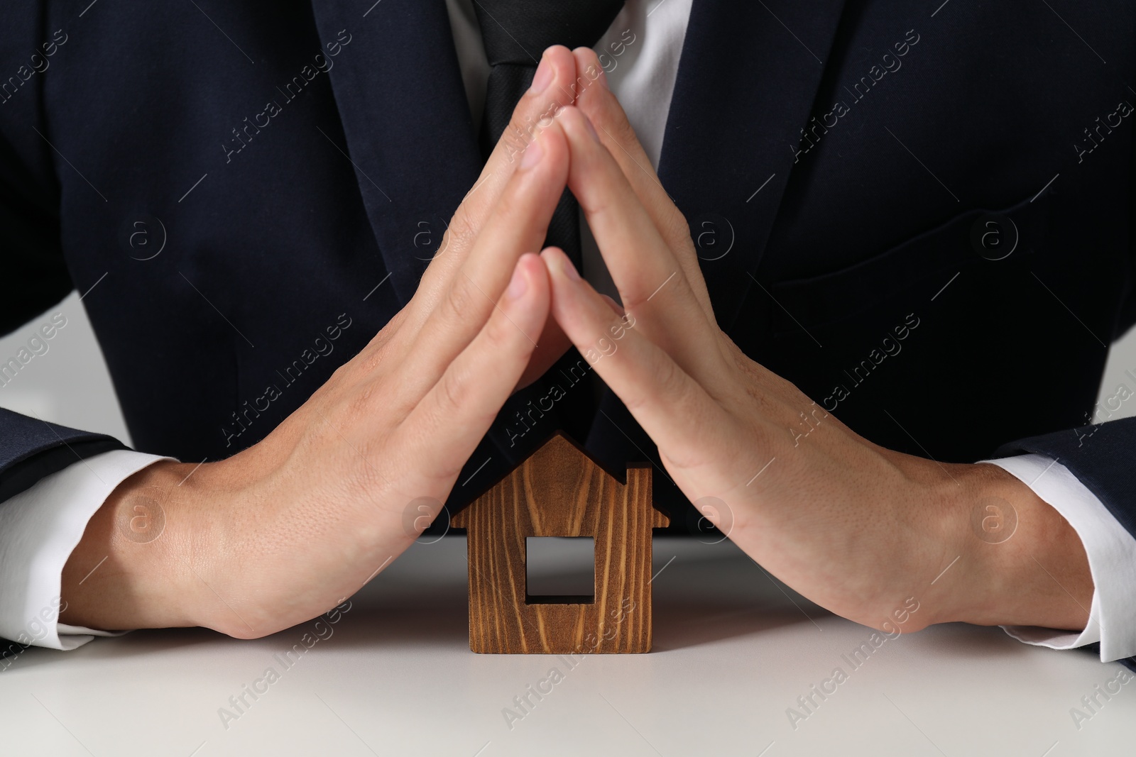 Photo of Real estate insurance. Man with wooden house figure at light table, closeup