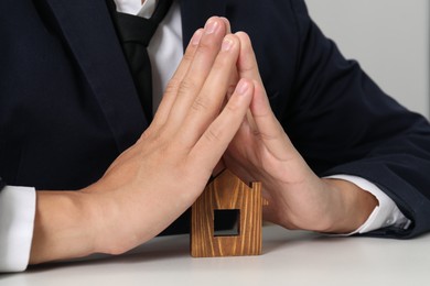 Photo of Real estate insurance. Man with wooden house figure at light table, closeup