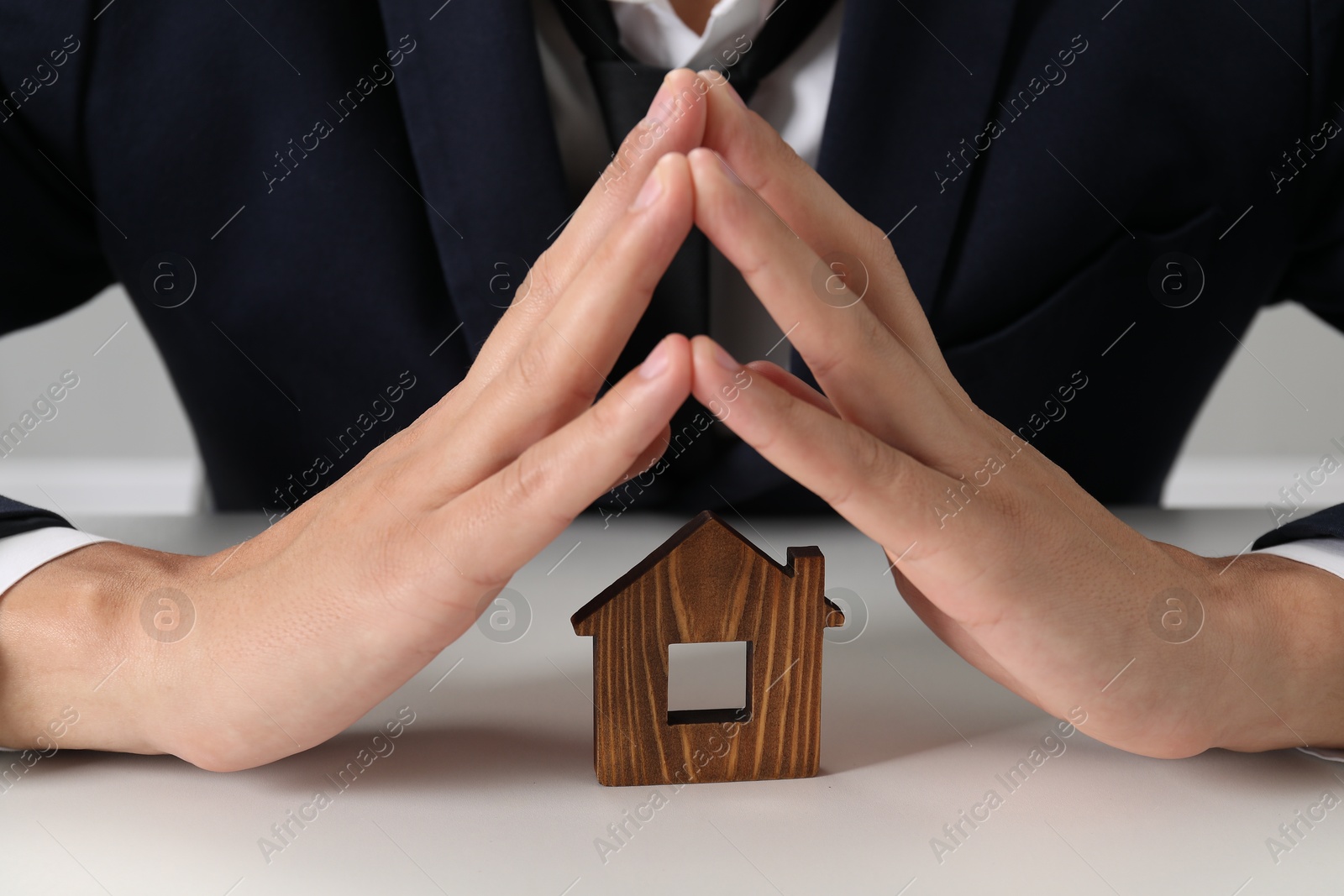 Photo of Real estate insurance. Man with wooden house figure at light table, closeup