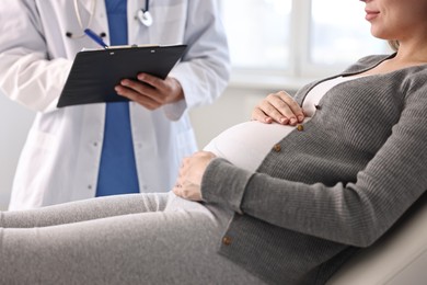 Doctor with clipboard consulting pregnant patient in clinic, closeup