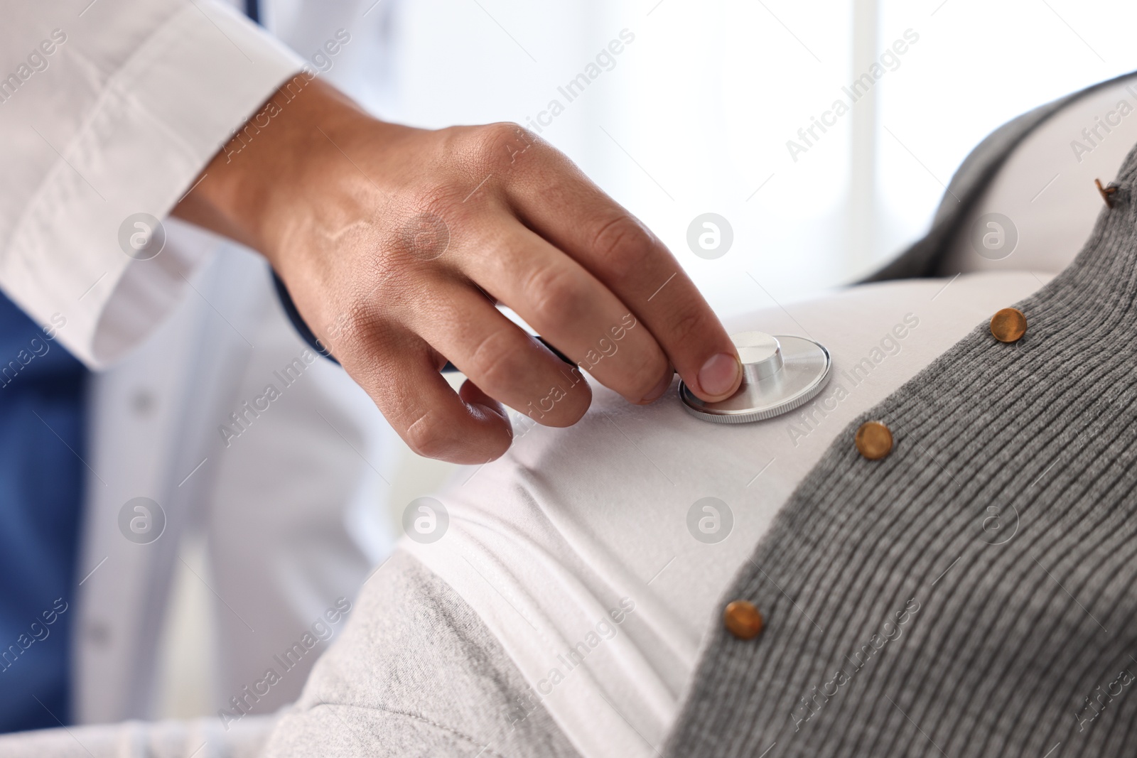 Photo of Pregnancy checkup. Doctor with stethoscope listening baby's heartbeat in patient's tummy indoors, closeup